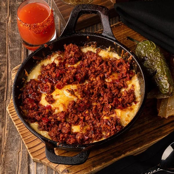 Okay Maguey's melted cheese with chorizo in a cast iron skillet, with a drink and jalapeño.