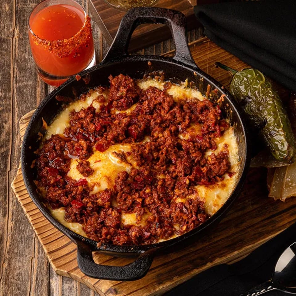 Okay Maguey's melted cheese with chorizo in a cast iron skillet, with a drink and jalapeño.
