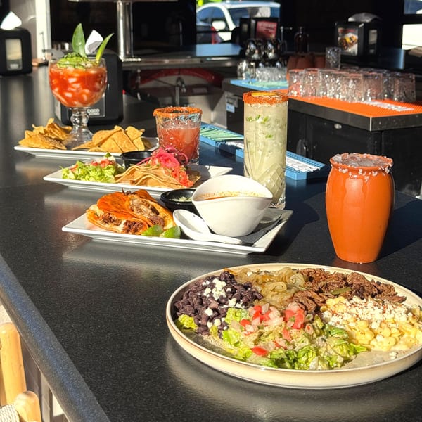 A bar counter with various Mexican dishes, including tacos, nachos, and a large bowl with different toppings.