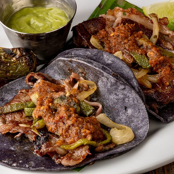 Okay Maguey's blue corn tacos with meat, peppers, onions, salsa, and a side of green sauce.