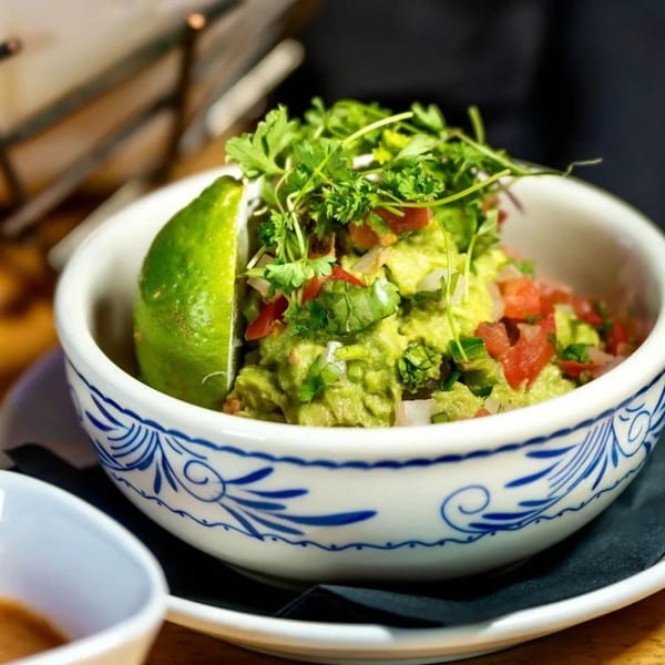 Okay Maguey's guacamole in a decorative bowl, garnished with cilantro, diced tomatoes, and a lime wedge.