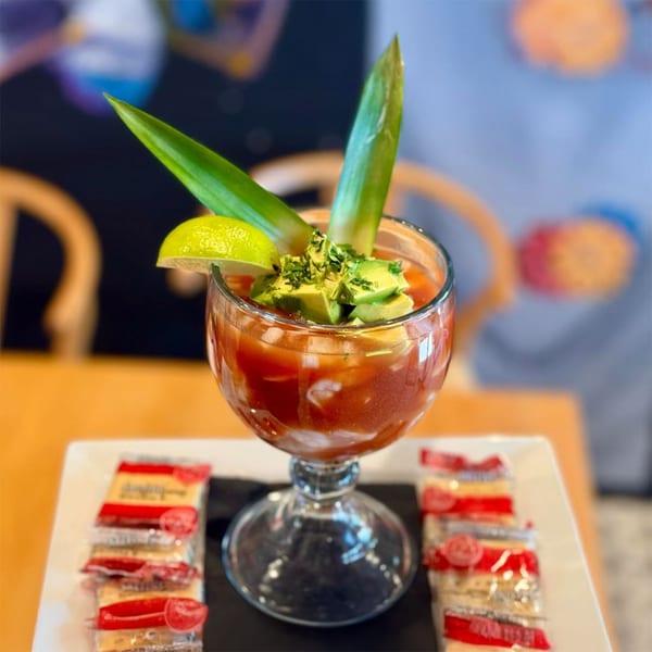 Okay Maguey's Mexican shrimp cocktail with avocado, lime, and crackers on a white plate.