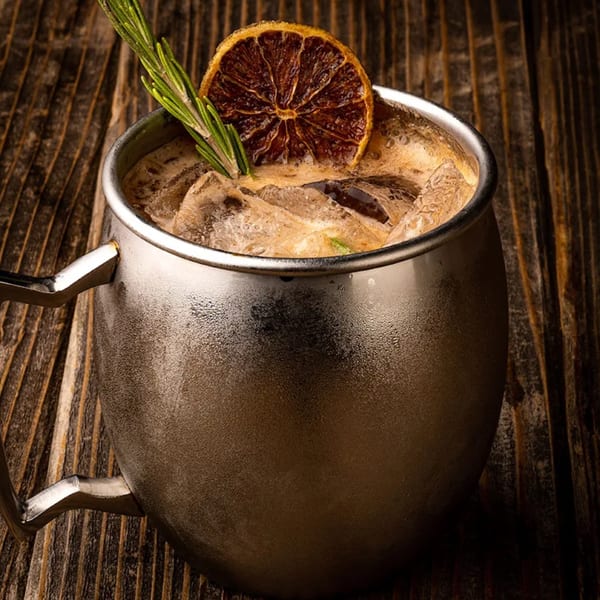 Okay Maguey's iced cocktail in a metal mug, garnished with rosemary and a dried orange slice.