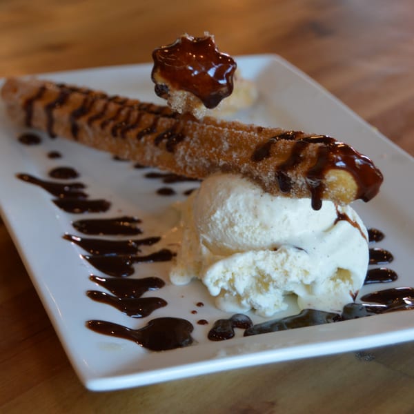 A churro with chocolate drizzle and a scoop of vanilla ice cream on a white plate.