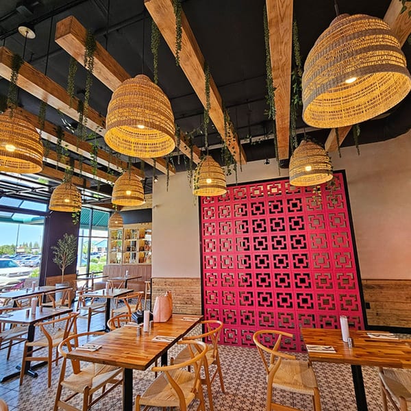 Okay Maguey dining room with wooden tables, woven chairs, wicker lamps, and a bright pink decorative wall.