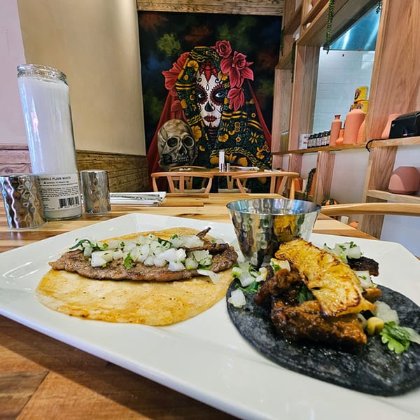 Two Mexican tacos, one with steak and onions, the other with pork and pineapple, on a white plate.