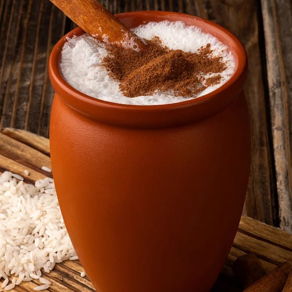Horchata in a clay mug, topped with cinnamon powder and a cinnamon stick, with rice grains.